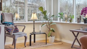 Een kamer met een groot raam, een stoel, een bijzettafeltje en een plant in pot.