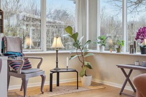 Una habitación con un ventanal grande, una silla, una mesita y una planta en maceta.