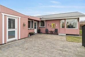 A pink building with a tiled roof, a patio with two chairs and a table, and a window with a decorative item.