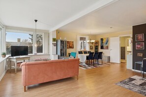 A spacious living area with a sofa, dining table, chairs, and a TV.