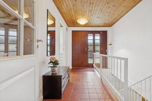 A hallway with wooden ceiling, white walls, a wooden door, and a white railing.