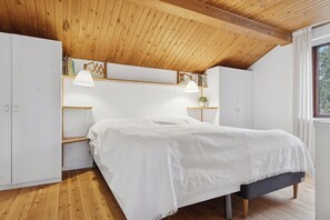 A bedroom with a wooden ceiling, white wardrobe, bedside lamps, and a bed with a white bedspread.