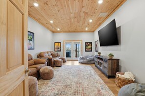 A cozy living room with a wooden ceiling, leather sofas, a flat-screen TV, and a large window. - Modern Smoky Mountain Home w/ Hot Tub, Game Room, Theater, Sleeps 12 (Sevierville)