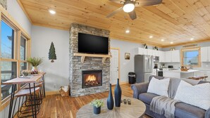 Un soggiorno moderno con camino in pietra, soffitto in legno e un grande televisore montato sopra.