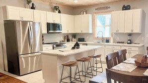 Una cucina moderna con mobili bianchi, elettrodomestici in acciaio inossidabile, un'isola centrale con sgabelli da bar e un tavolo da pranzo in legno.