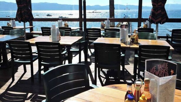 Ett utomhusområde med bord och stolar, utsikt över vattnet och en skylt för Lake Tahoe Works Club.