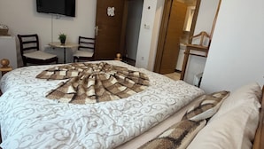 Un dormitorio con una cama grande, un televisor montado en la pared, una mesita con sillas y una puerta de madera.