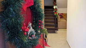 Un pasillo con un adorno navideño en una puerta de madera, una escalera al fondo y una pared blanca.