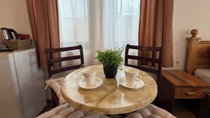 Un comedor con una mesa redonda de mármol, dos sillas con cojines, una planta en maceta y un refrigerador pequeño.