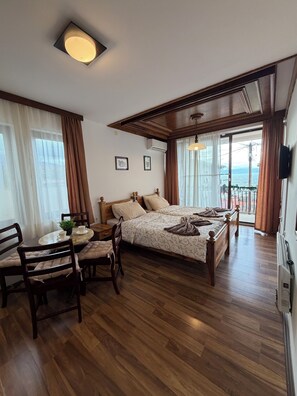 A bedroom with a wooden floor, a bed with a headboard, a bedside table with a plant, and a window with curtains. - Ohrid Villa Srma (Ohrid)