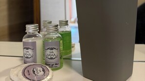 Una encimera de baño con una taza gris, tres pequeñas botellas de jabón líquido y un cepillo de dientes en un soporte de plástico.