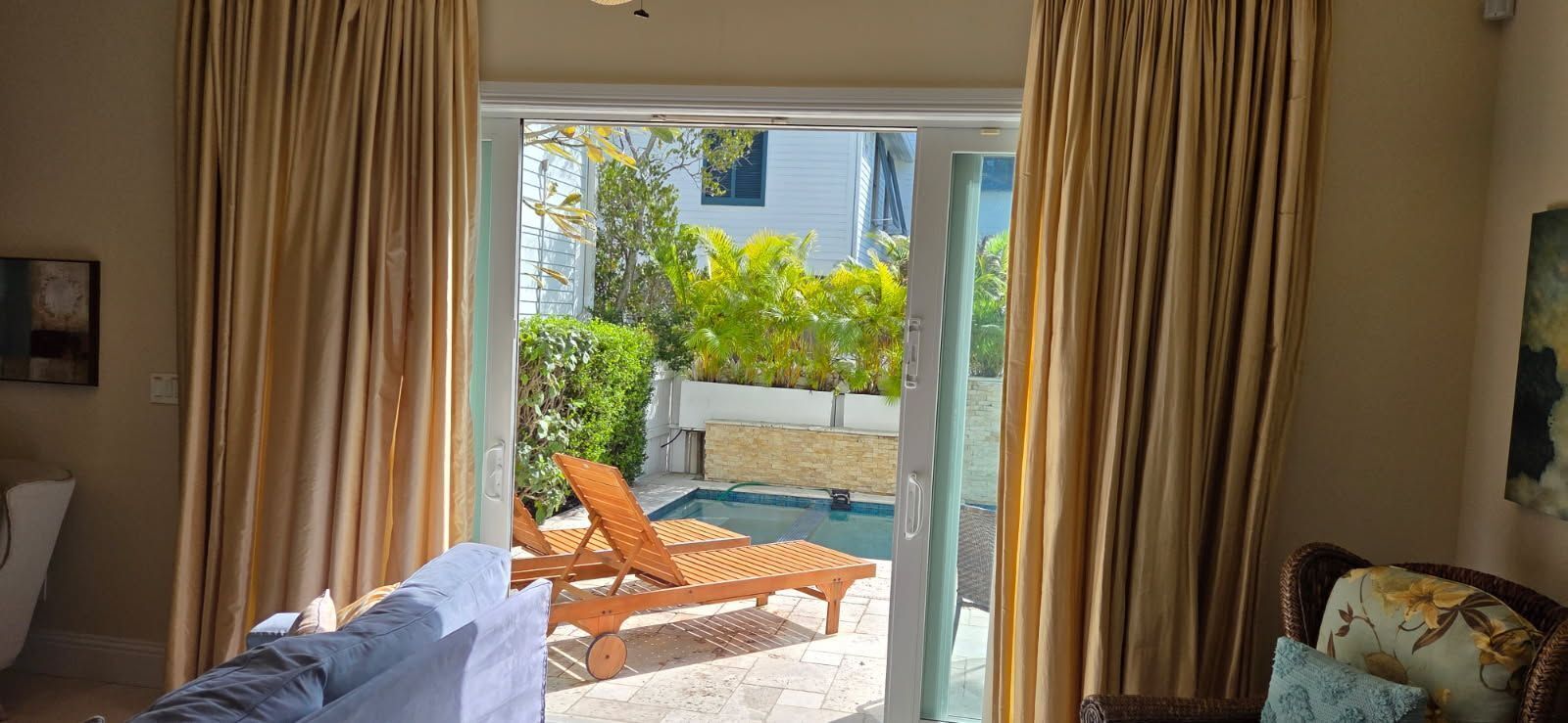 A room with a sliding glass door leading to a pool area, a chair, and a bed with a white cover.