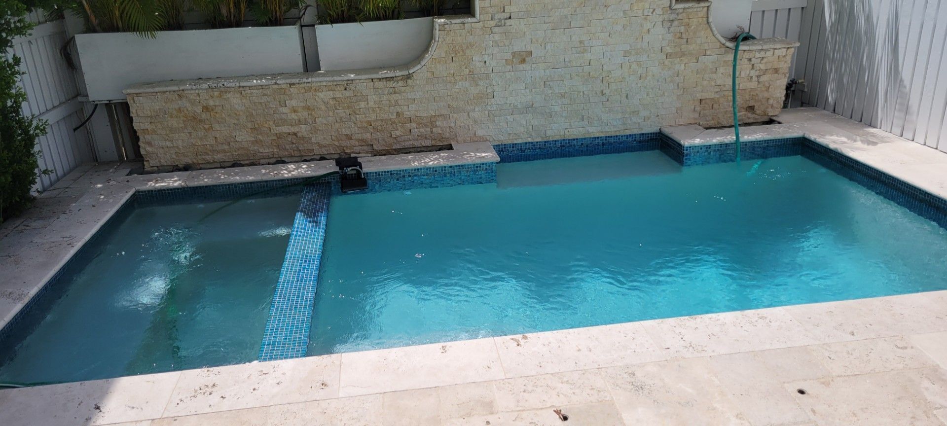 A rectangular swimming pool with a tiled edge and a stone wall backdrop.