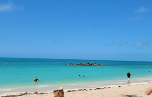 Uma praia com águas turquesa cristalinas, um afloramento rochoso e pessoas nadando e andando na costa.
