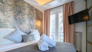 Una camera da letto con un letto, cuscini, una televisione e una finestra con tende.