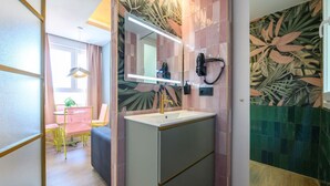 Un bagno con lavandino, specchio e asciugacapelli. Nell'ambiente adiacente, una sedia e un tavolo.