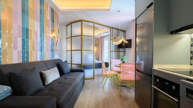 Una cucina moderna con forno integrato, un'area pranzo con tavolo e sedie, e un soggiorno con divano e parete decorata da un'opera d'arte astratta e colorata.
