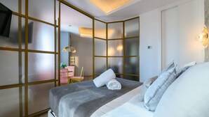 Una camera d'albergo moderna con un letto grande, una scrivania con una sedia e vista separata da un pannello con cornice dorata.