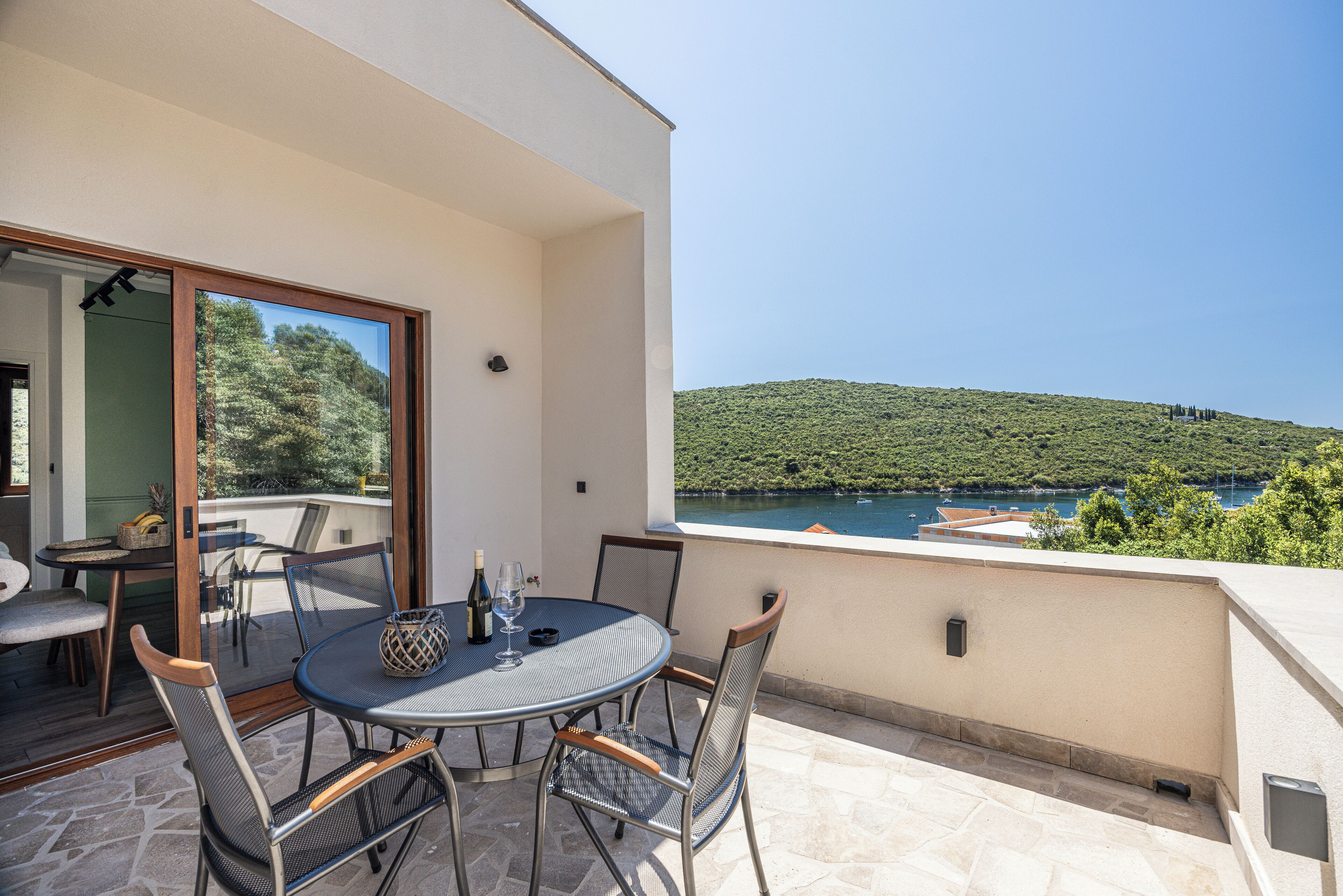 A balcony with a table and chairs, overlooking a scenic view of a lake and hills.