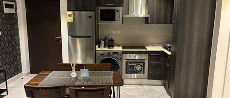 Cocina moderna con armarios oscuros, electrodomésticos de acero inoxidable y un comedor con mesa de vidrio y sillas de madera.