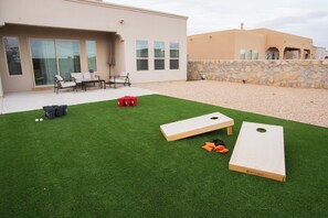 A backyard with artificial grass, two wooden bean bags, and a stone wall.