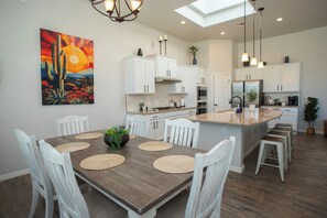 Een moderne keuken met witte kasten, een centraal eiland en een eethoek met een houten tafel en witte stoelen.