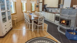 Un intérieur en bois comprenant une table à manger, des chaises, une cuisine avec une cheminée en pierre et un buffet aux portes vitrées.