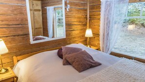Une chambre à coucher dans un chalet en bois, avec un lit, un miroir, deux lampes de chevet et une fenêtre avec des rideaux.