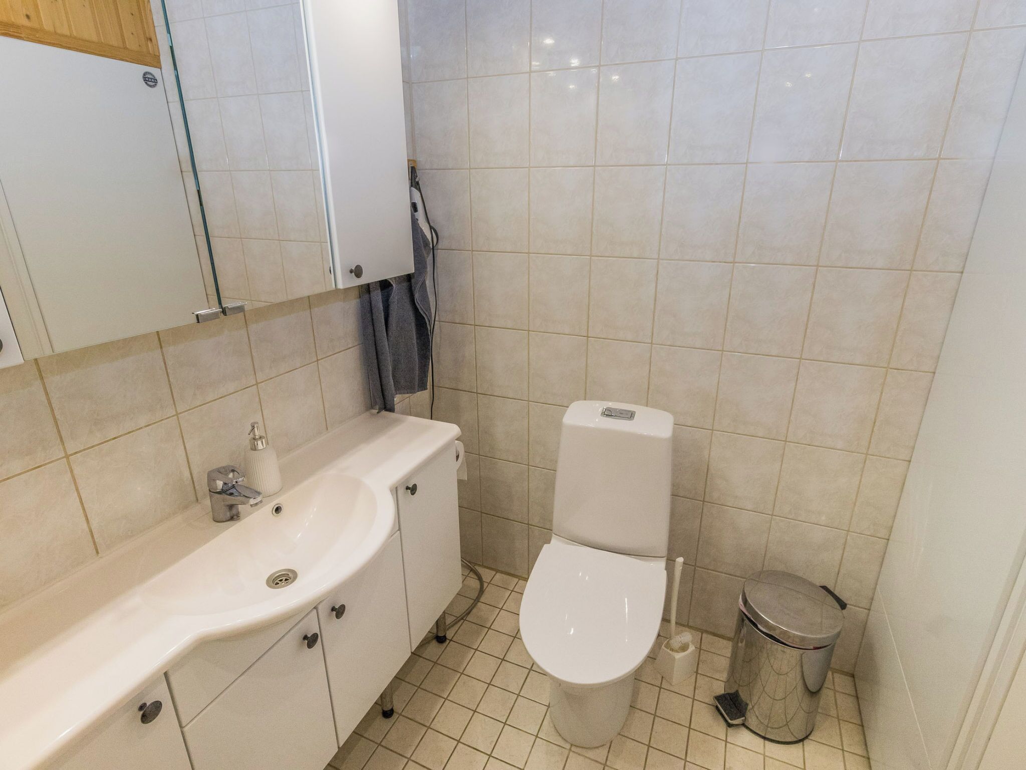 A bathroom with a white sink, toilet, and trash can.