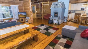 L’intérieur chaleureux d’un chalet avec un plancher en bois, une cheminée en pierre, un coin repas et un salon comprenant un canapé et un téléviseur.