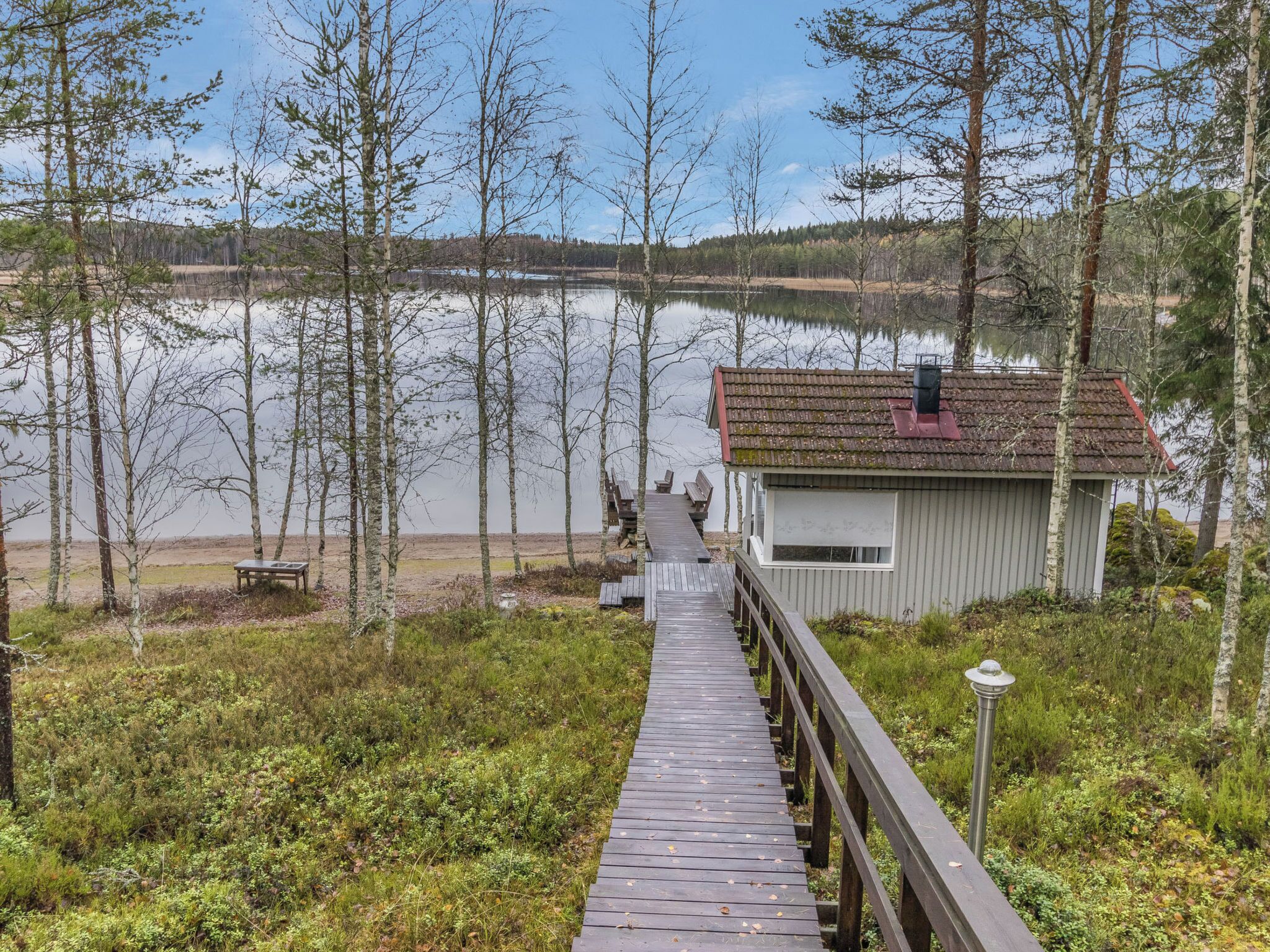 Une promenade en bois mène à une petite cabane située au bord d’un lac, entourée d’arbres.
