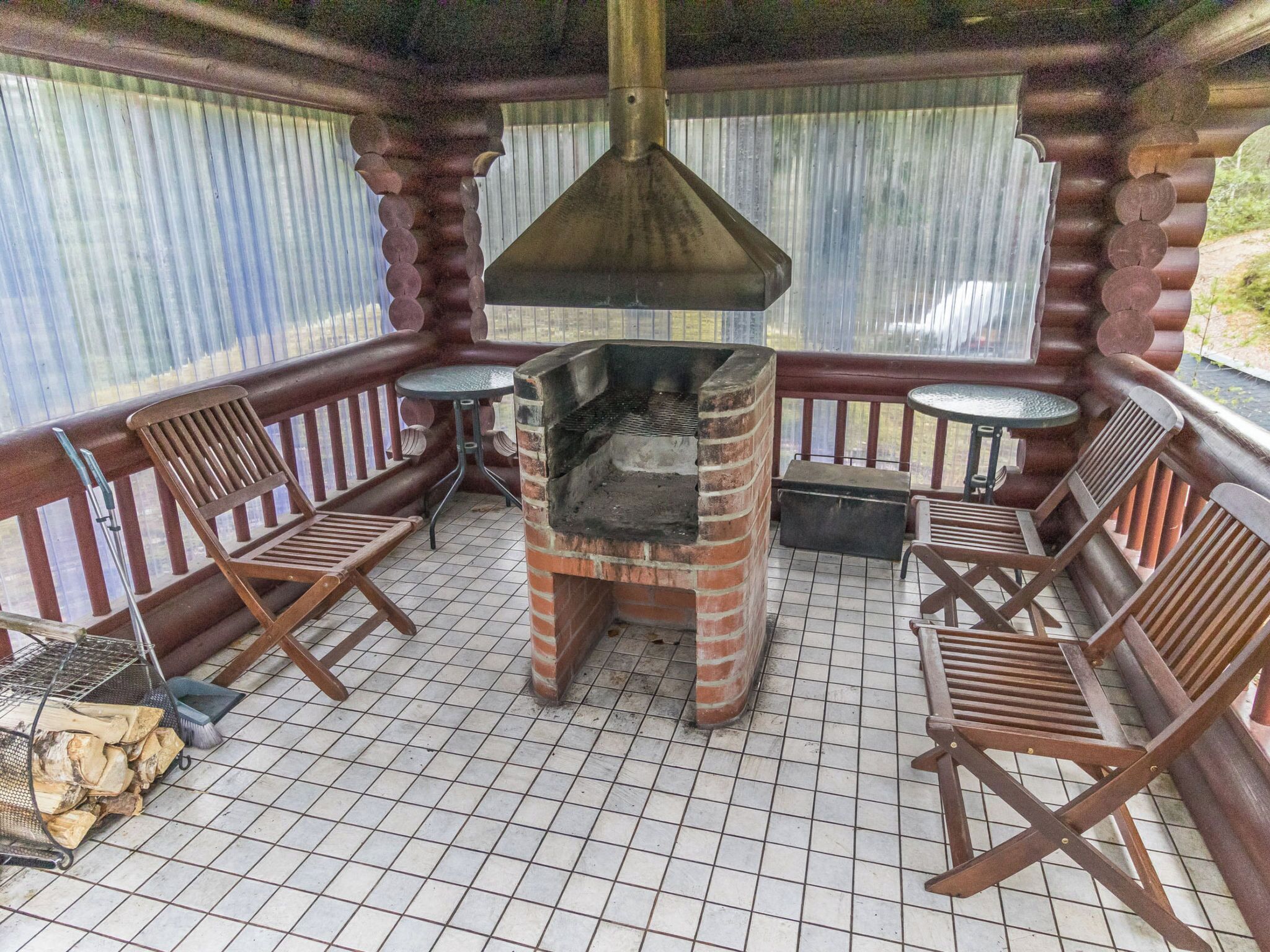Une terrasse couverte avec un four à pizza en briques, des chaises en bois et une petite table.