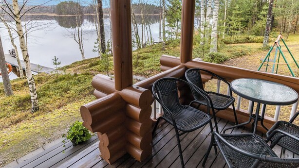 A wooden deck with outdoor seating, overlooking a lake and forested area. - Villa maaria by Interhome (Juva)