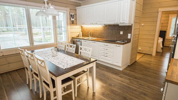 Een moderne keuken met witte kastjes, een houten eettafel en uitzicht op de omgeving door grote ramen.
