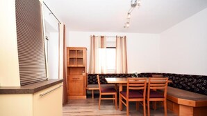 Een kleine keuken met een eethoek, houten kastjes, een ingebouwde bank en een raam met gordijnen.