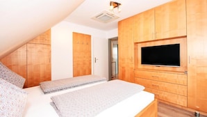 Een slaapkamer met een schuine kap, een houten garderobe, een flatscreen-televisie en een bed met beddengoed met een patroon.
