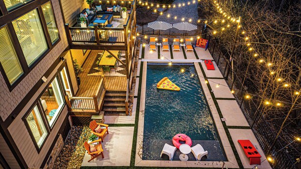 A rooftop pool area with a floating pizza slice, lounge chairs, and string lights.