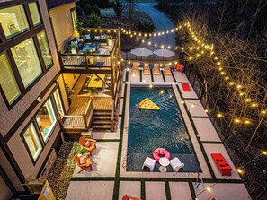A rooftop pool area with a floating pizza slice, lounge chairs, and string lights. - HGTV-Designed AVL Retreat · Sauna, HotTub, Theater, Fire , Elevator · Sleeps 20 (Asheville)