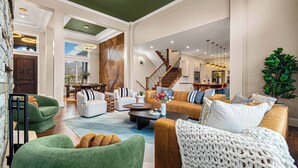 A spacious living room with a staircase, green and brown sofas, a coffee table, and a large plant.