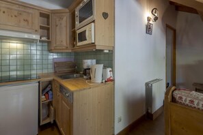 Eine kompakte Küche mit Holzschränken, einer Mikrowelle, einem Toaster und einem kleinen Kühlschrank.