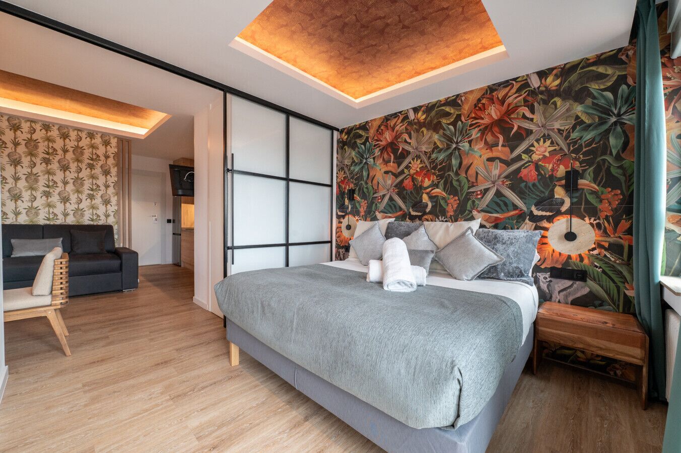 A modern bedroom with a large bed, a wooden floor, a floral wallpaper, and a ceiling light.