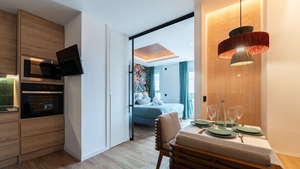 A modern kitchen with built-in appliances, a dining area with a table set for two, and a bedroom with a bed and a view of the outdoors. - GRAN VIA capitals, MADAGASCAr (Madrid)