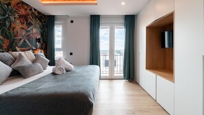 A modern bedroom with a large bed, a mural on the wall, a balcony with curtains, and a TV mounted on the wall. - GRAN VIA capitals, MADAGASCAr (Madrid)