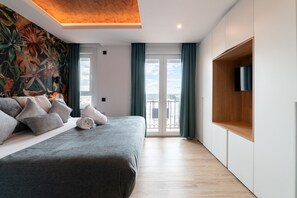 A modern bedroom with a large bed, a mural on the wall, a balcony with curtains, and a TV mounted on the wall. - GRAN VIA capitals, MADAGASCAr (Madrid)
