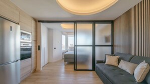 A modern kitchen with built-in appliances, a sliding glass door leading to a balcony, and a grey sofa with cushions. - GRAN VIA capitals,ISLAS MAURICiO (Madrid)