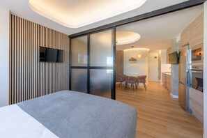 Quarto de hotel moderno com cama, área de refeições e cozinha.