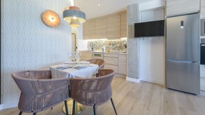 A modern kitchen with a built-in refrigerator, wooden cabinets, and a dining area with wicker chairs and a table set for two. - GRAN VIA capitals,ISLAS MAURICiO (Madrid)