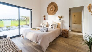 A modern bedroom with a large bed, a view of the outdoors, and a shower area.
