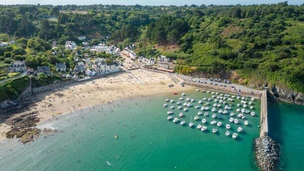 An aerial view of a coastal town with a beach, a marina with boats, and residential buildings.