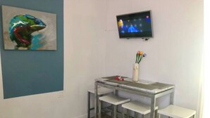 Ein Zimmer mit Schreibtisch, zwei Stühlen, einem an der Wand befestigten Fernseher und einem Bild.